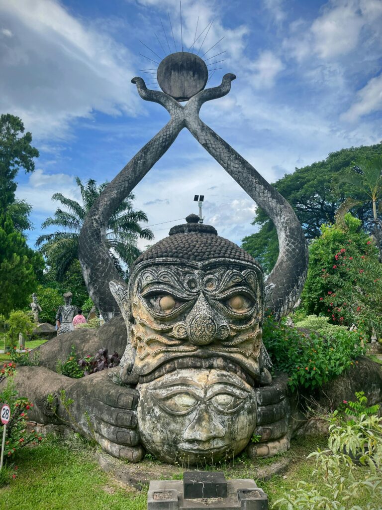 Intricate stone sculpture in lush park setting under a clear blue sky.