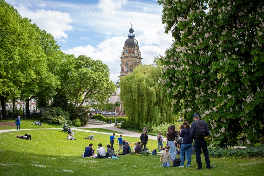 Visitors enjoy a sunny day in Planten un Blomen park, Hamburg, with scenic greenery and iconic architecture.