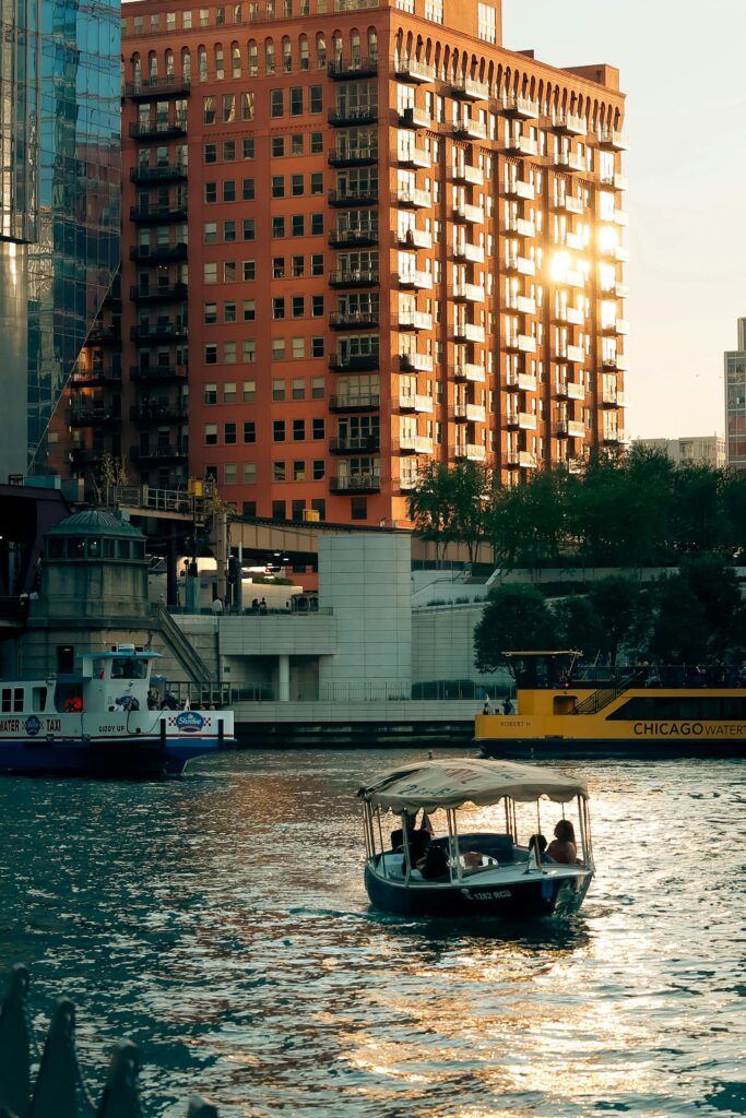 Boaters enjoy a scenic sunset river view with city skyline in background.