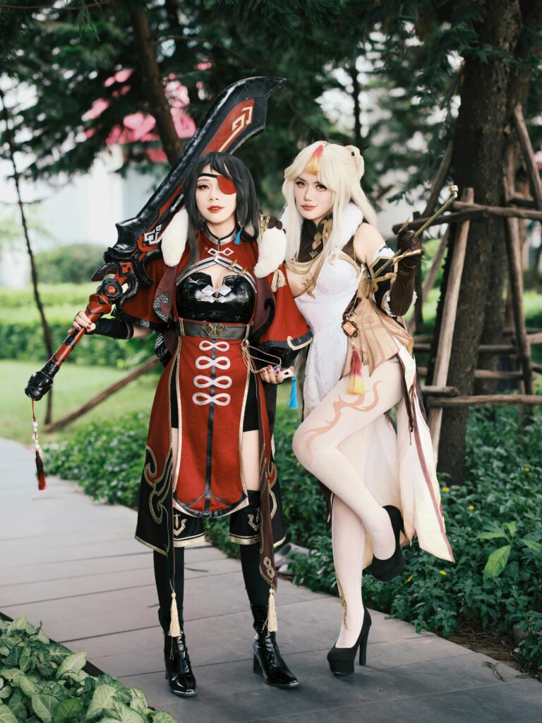 Two cosplayers demonstrating intricate fantasy costumes in an outdoor setting.