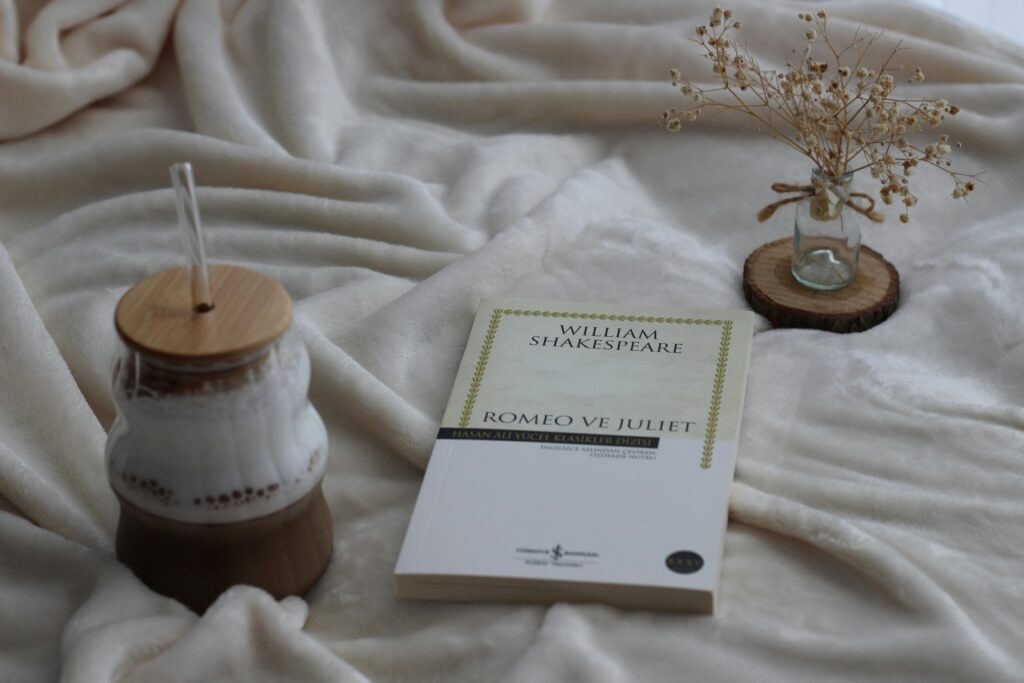 A cozy still life featuring a book, warm beverage, and dried flowers on a soft fabric.