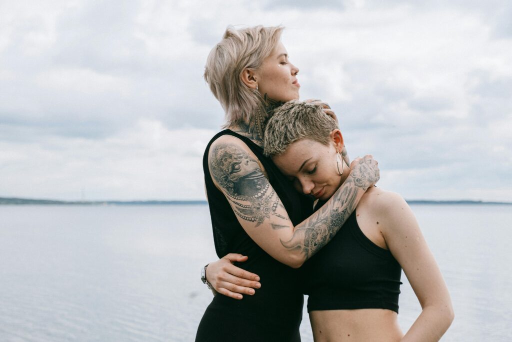 A tattooed couple shares an affectionate embrace by the seaside, showcasing love and trust.
