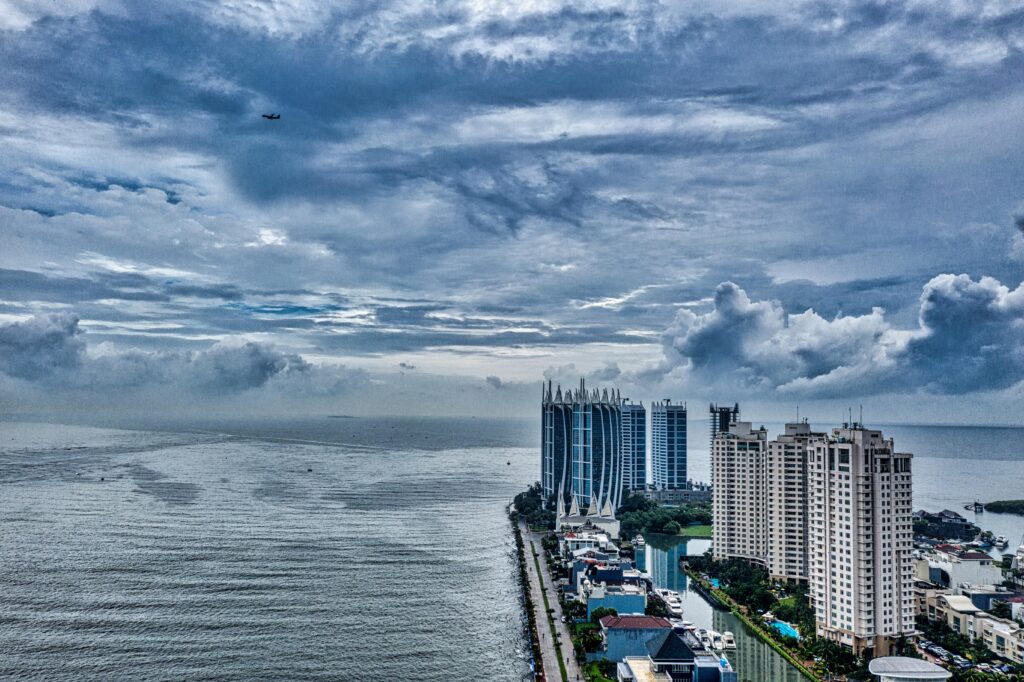 Aerial view of Jakarta's coastal skyline under dramatic cloudy skies, highlighting urban architecture.