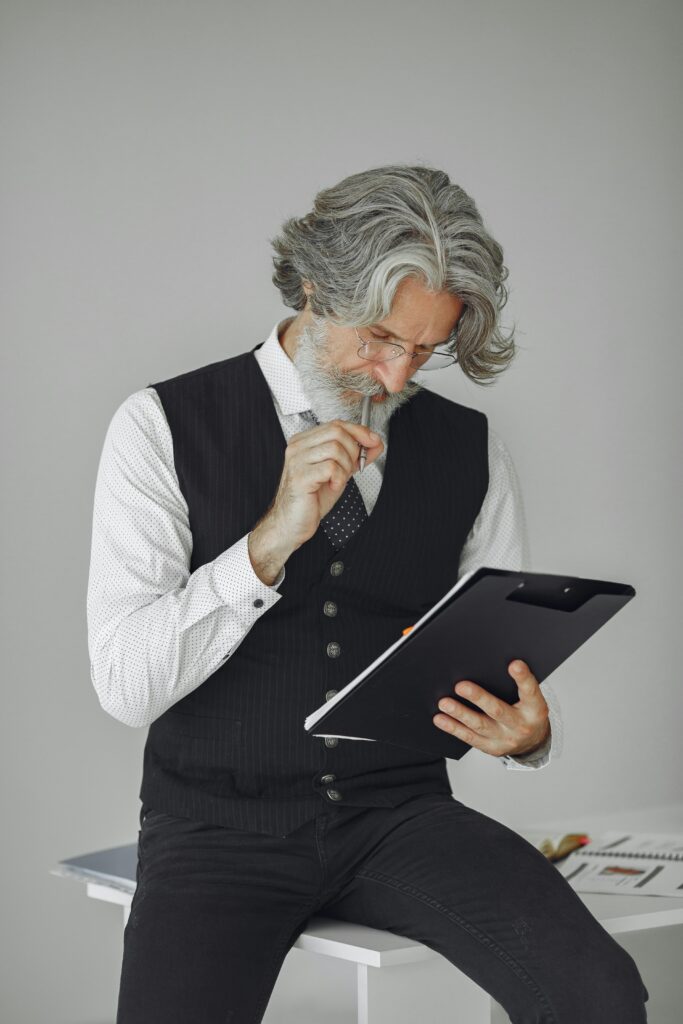 Senior man with gray hair examines papers on clipboard. Professional look.