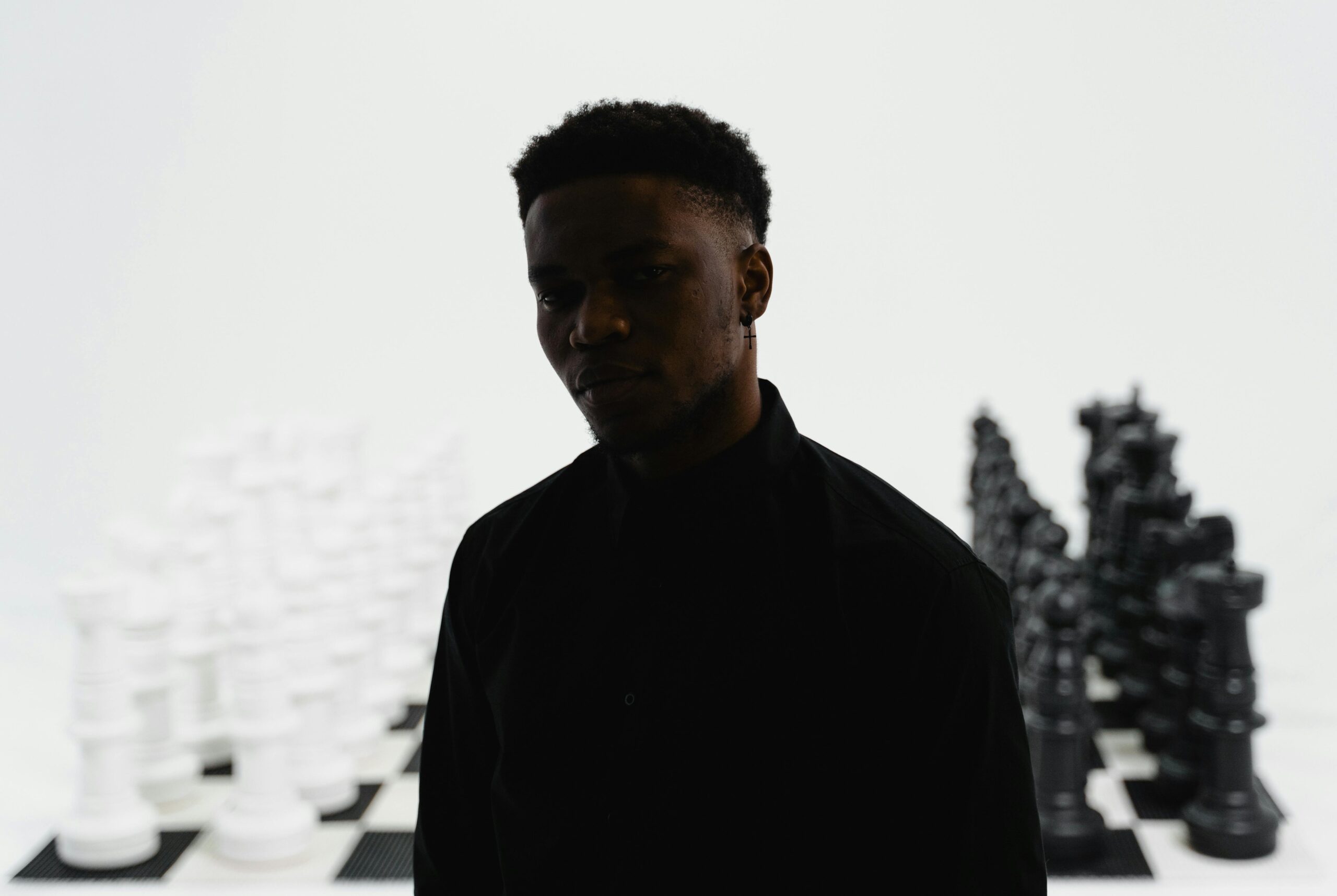 A man stands in front of a chessboard with life-sized pieces, creating a dramatic and serious ambiance.