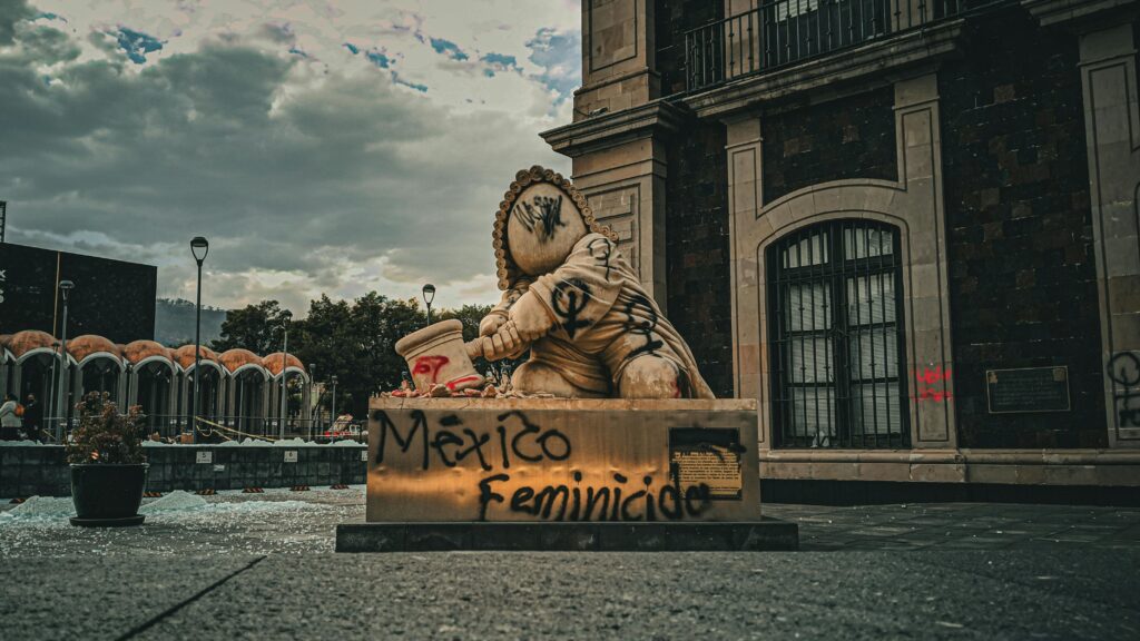 A statue in Mexico features bold graffiti including 'México' and 'Feminicidio', highlighting a protest message.