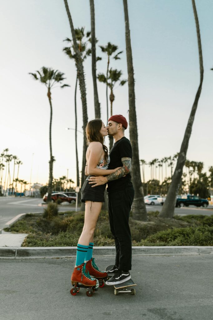 A vibrant young couple kisses on roller skates and skateboard at sunset in California.