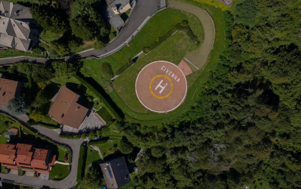 Drone shot capturing a helipad in Civenna surrounded by greenery and residential houses.