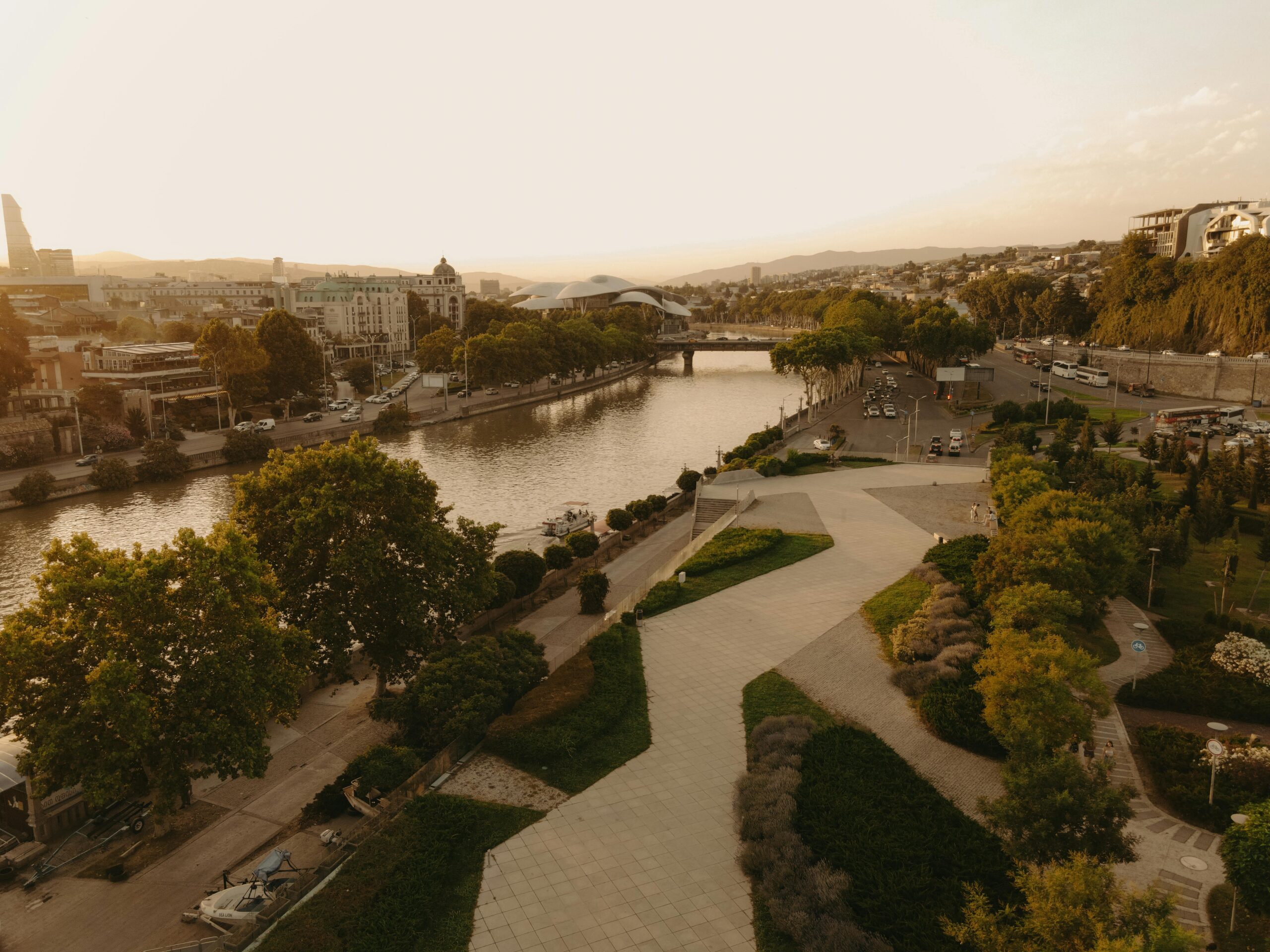 A stunning aerial view of Tbilisi, Georgia showcasing its riverfront, parks, and skyline at sunset.