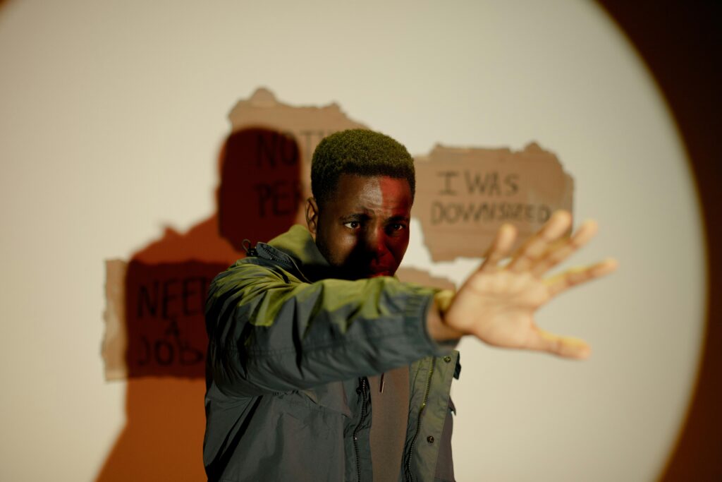 A man stands with an outstretched hand, conveying crisis and unemployment indoors.