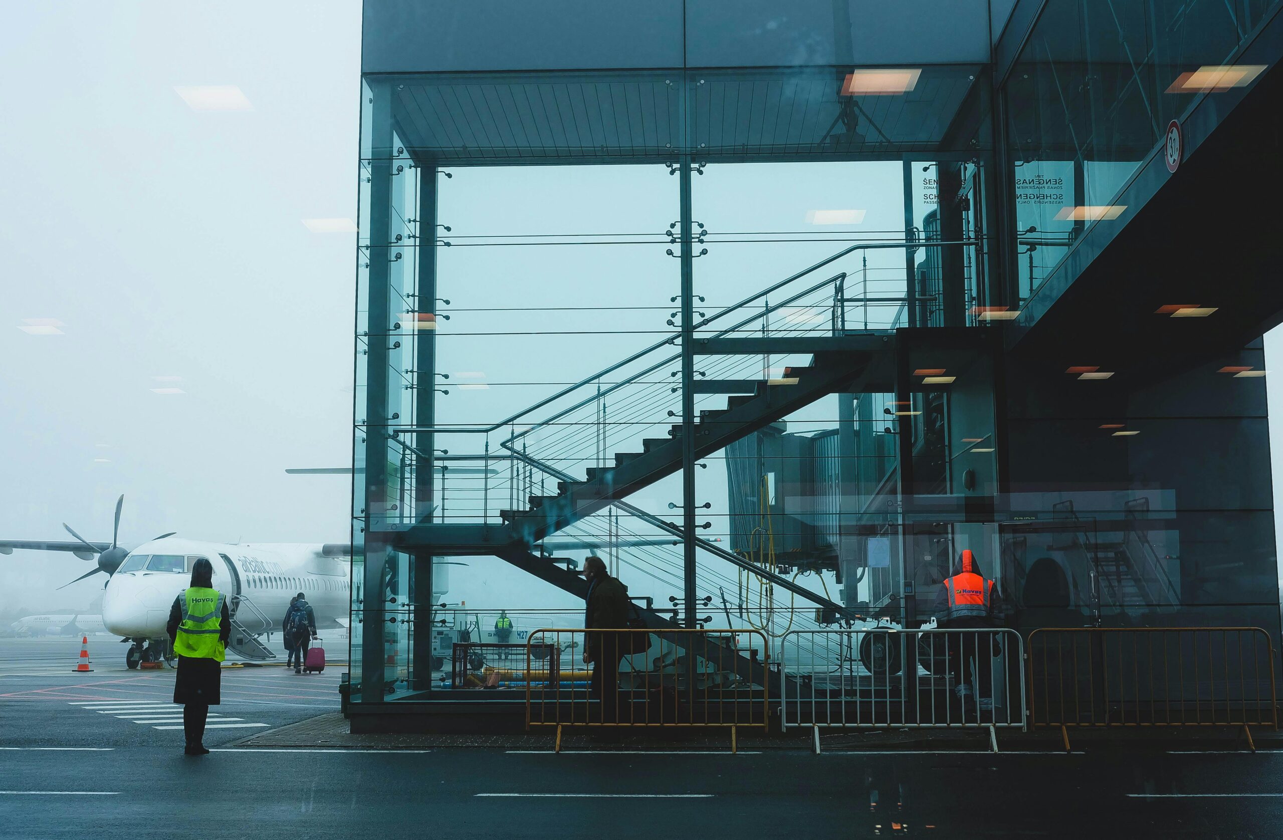 Passengers boarding an airplane at Riga Airport amidst fog, showcasing modern airport architecture.