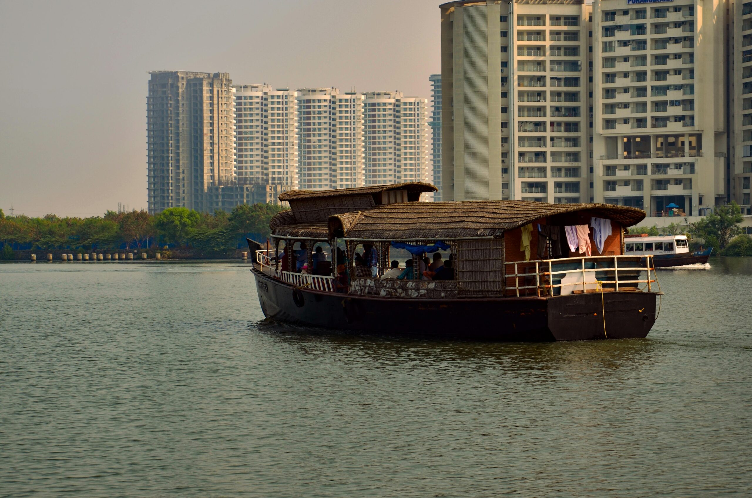 A picturesque scene of a traditional houseboat on a river with Kochi's modern skyline in the background.
