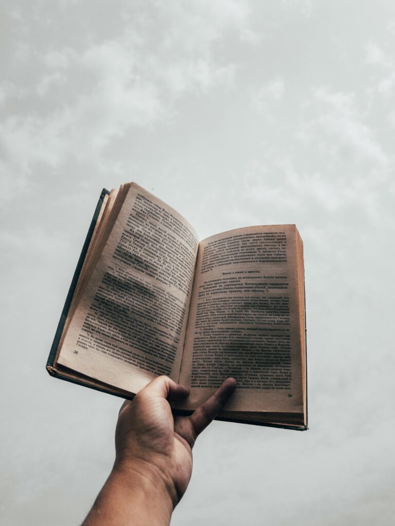 A hand holding an open book against a backdrop of cloudy sky, symbolizing knowledge and freedom.