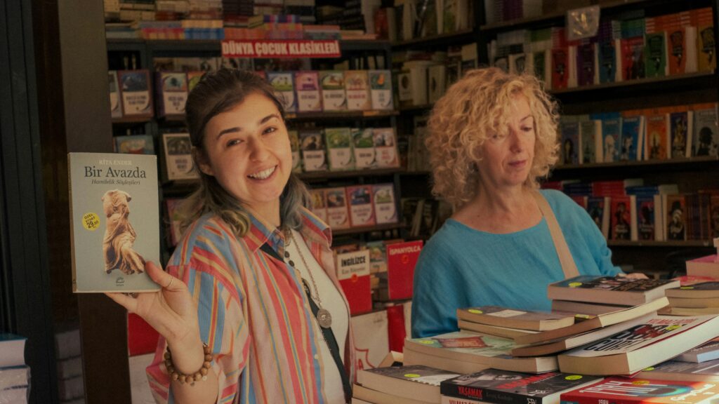 A young woman holding a book and smiling in a cozy bookstore setting.