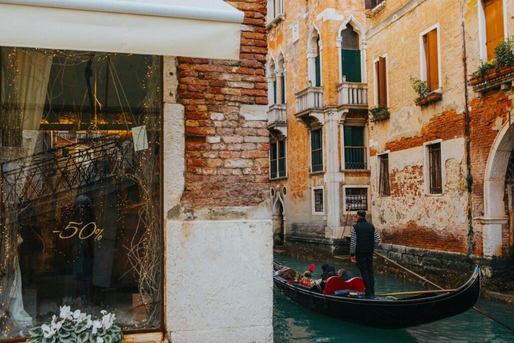 A gondola glides through the historic canals of Venice, Italy, past a shop offering 50% discounts.