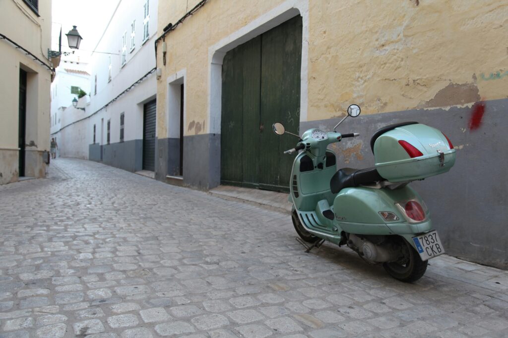 Discover the quaint charm of Ciudadela de Menorca with a classic Vespa on a cobblestone street.