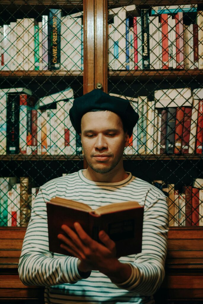 A man in a beret and striped shirt enjoys reading in a vintage library setting.