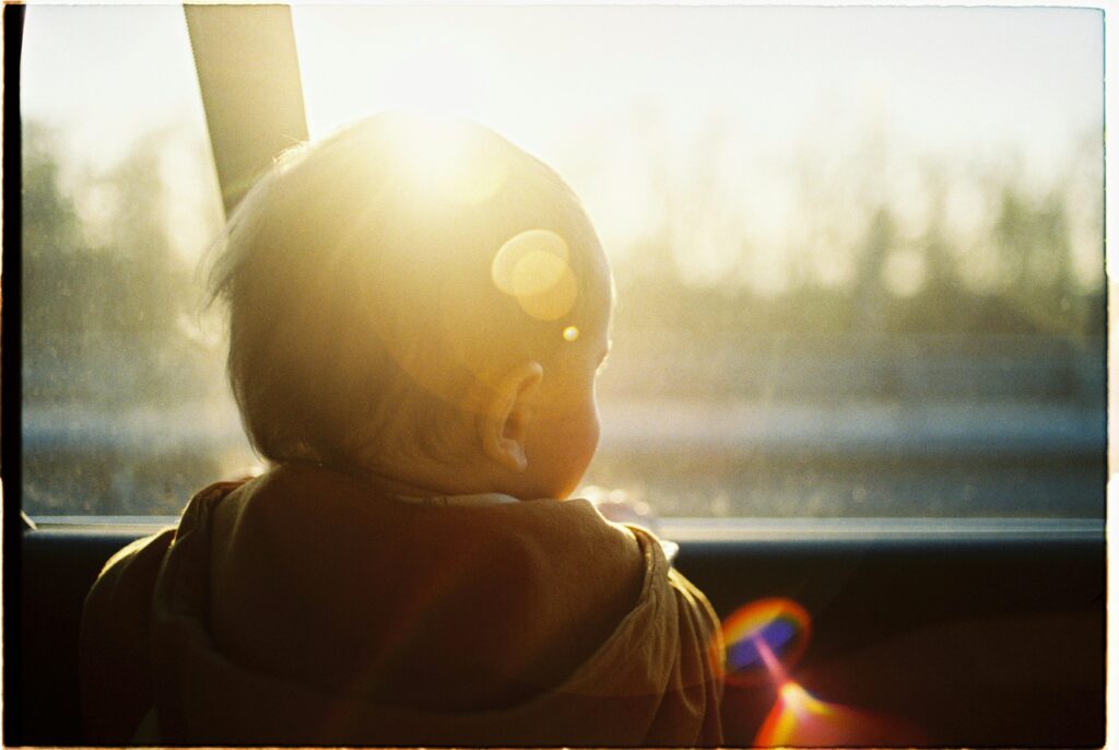 Serene backlit image capturing a baby gazing through a car window at sunset.