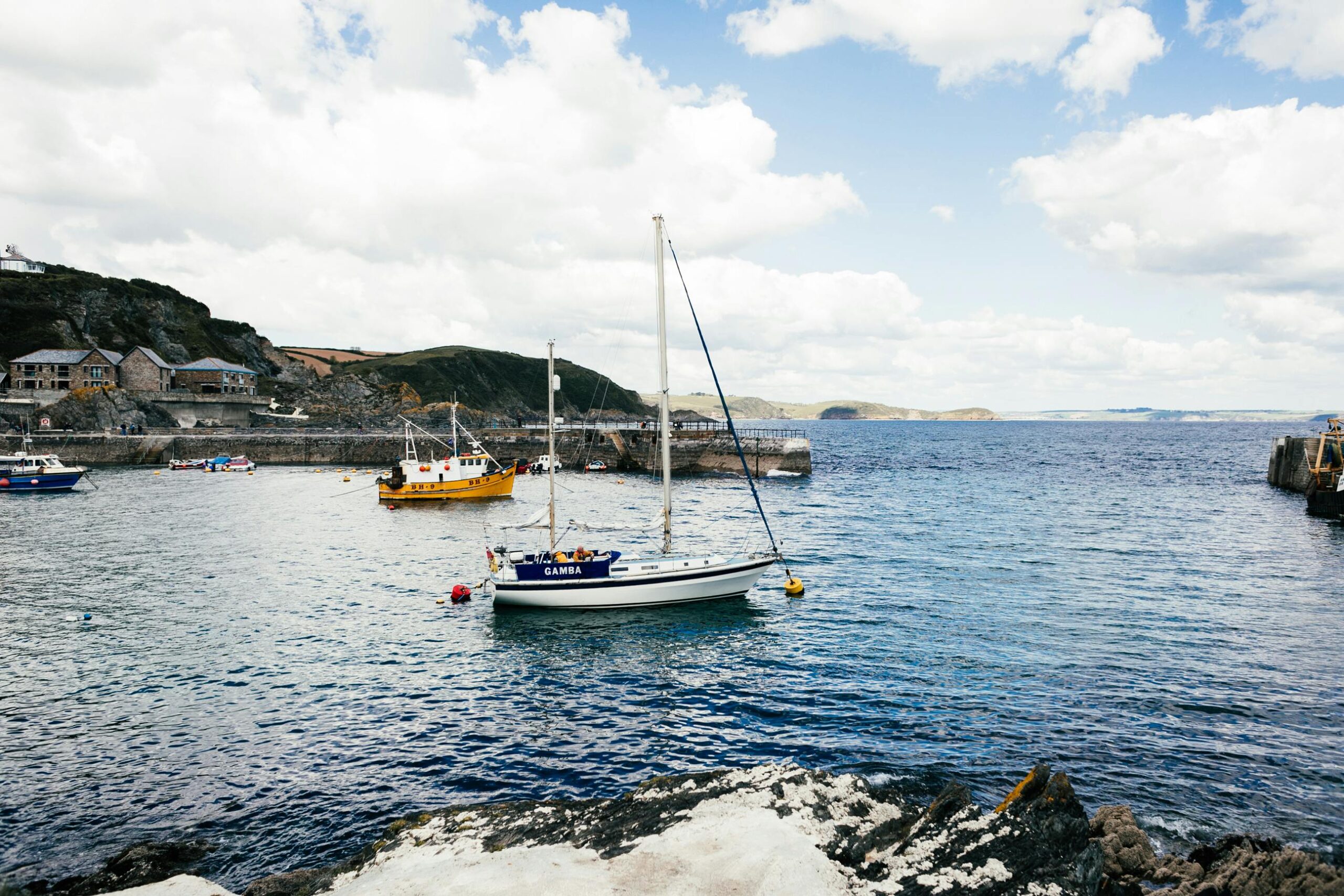 Serene view of sailboats docked at a scenic harbor in England under a partly cloudy sky.