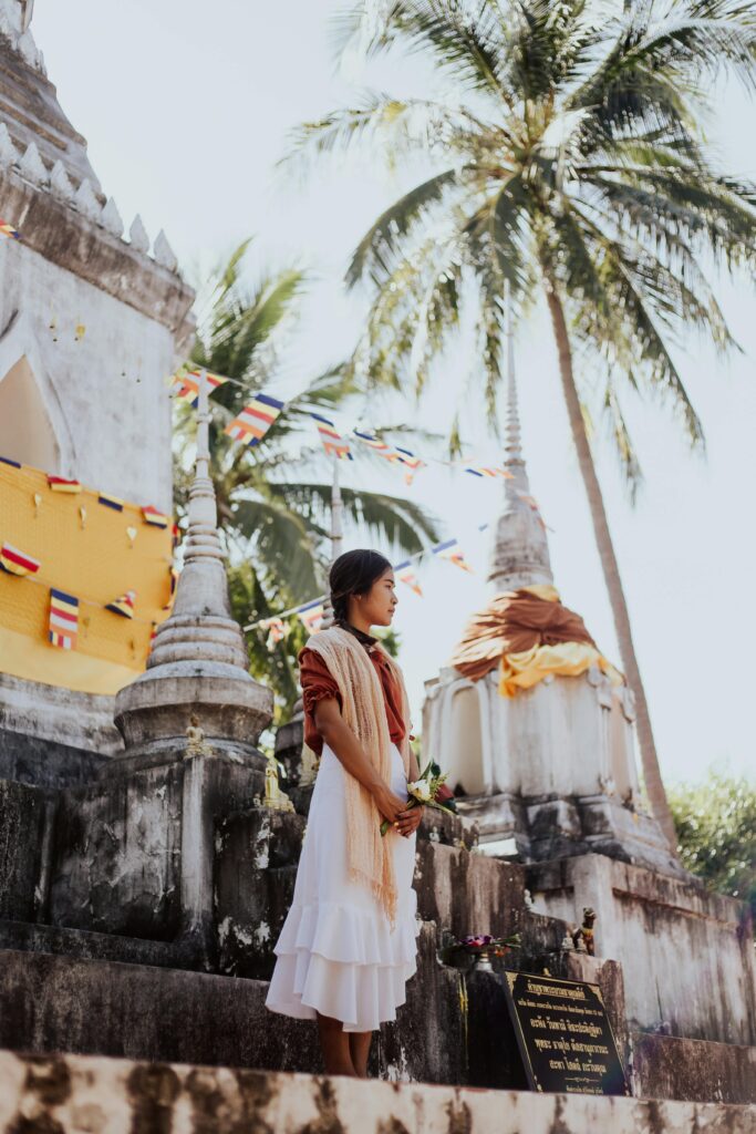 A woman in traditional clothing enjoys a peaceful moment near a historic Buddhist temple surrounded by palm trees.