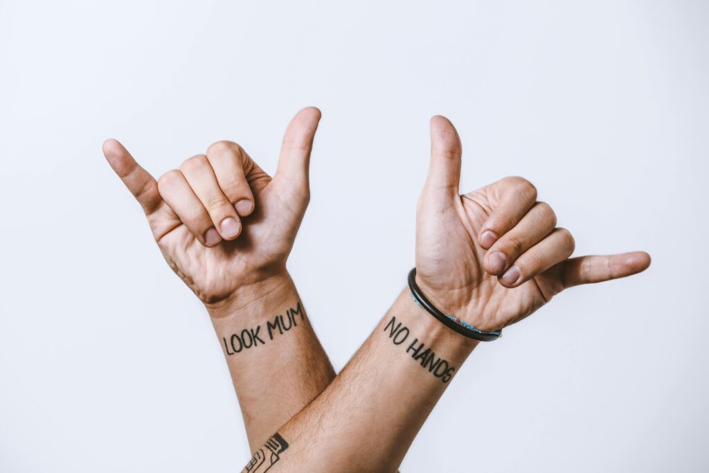 Crop anonymous male hands with creative look mum and no hands tattoo inscriptions showing shaka sign with fingers against white background