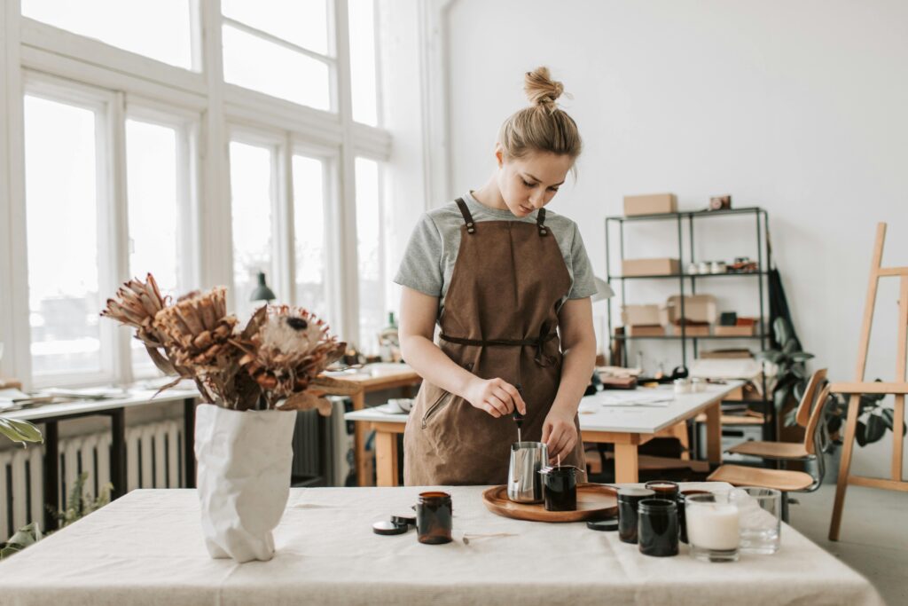 A woman craftsperson creating handmade candles in a bright, airy workshop.
