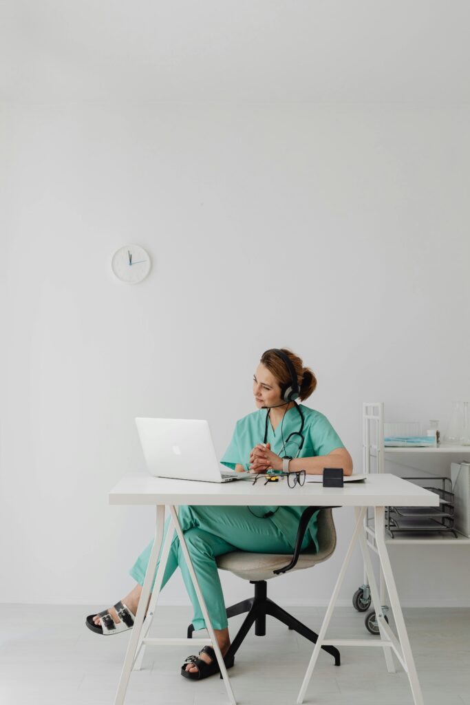 Healthcare professional in scrubs using laptop for telemedicine session in modern office.