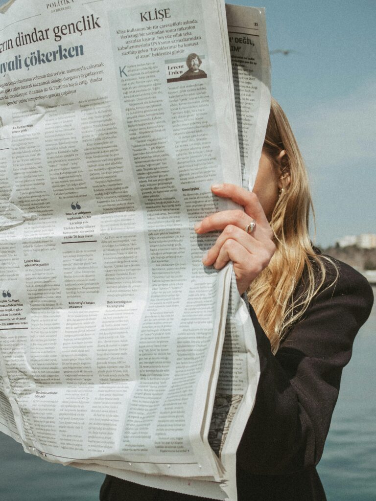 A woman in a black blazer reads a large newspaper by the water in Istanbul, Turkey.