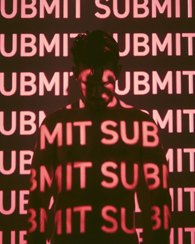 Dark silhouette against red repeating 'submit' text projection.