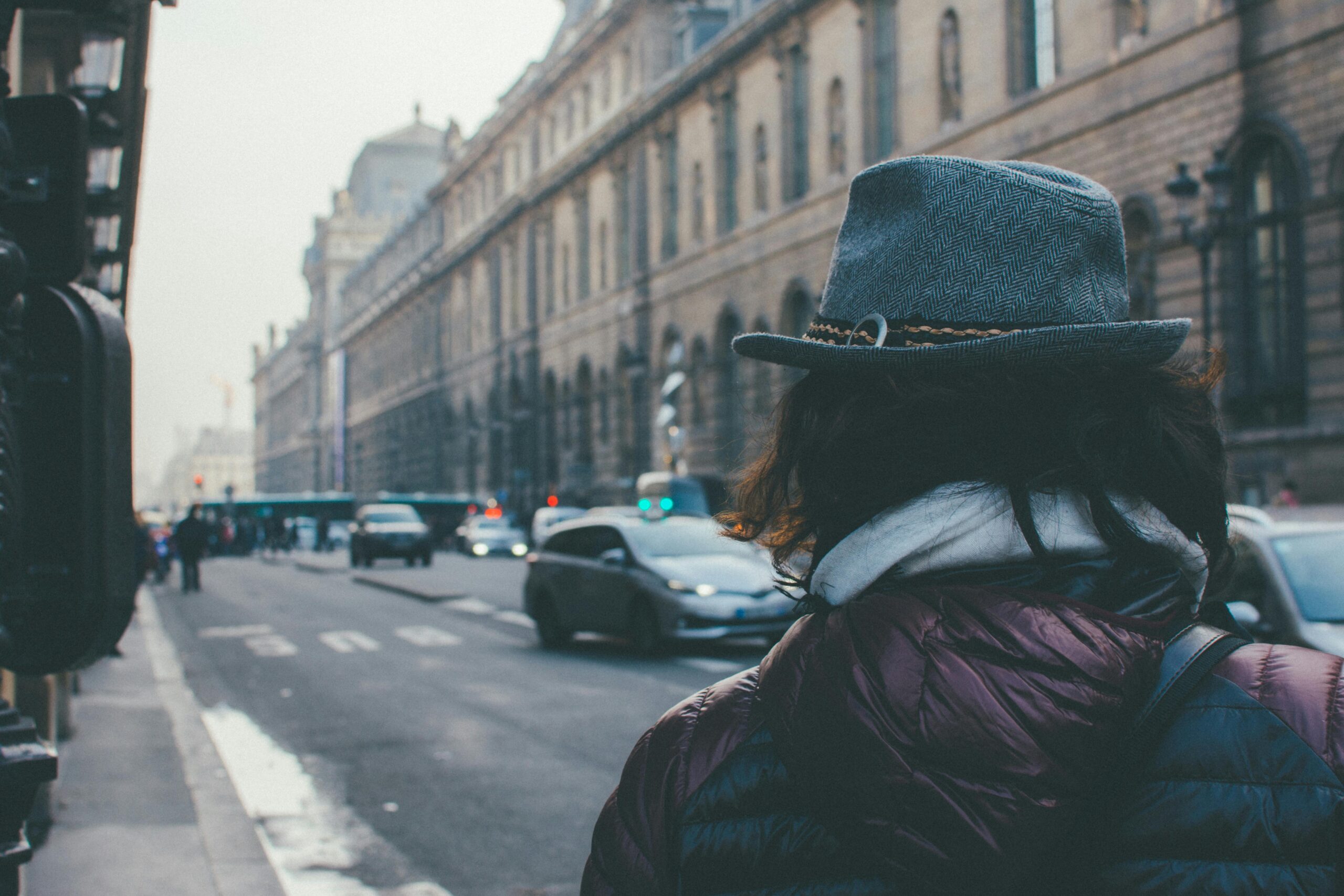 A person in a fashionable hat walks down a bustling street in Paris, France.