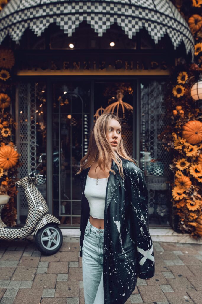 Fashionable woman in jeans and coat stands at the entrance of a stylish Istanbul cafe.