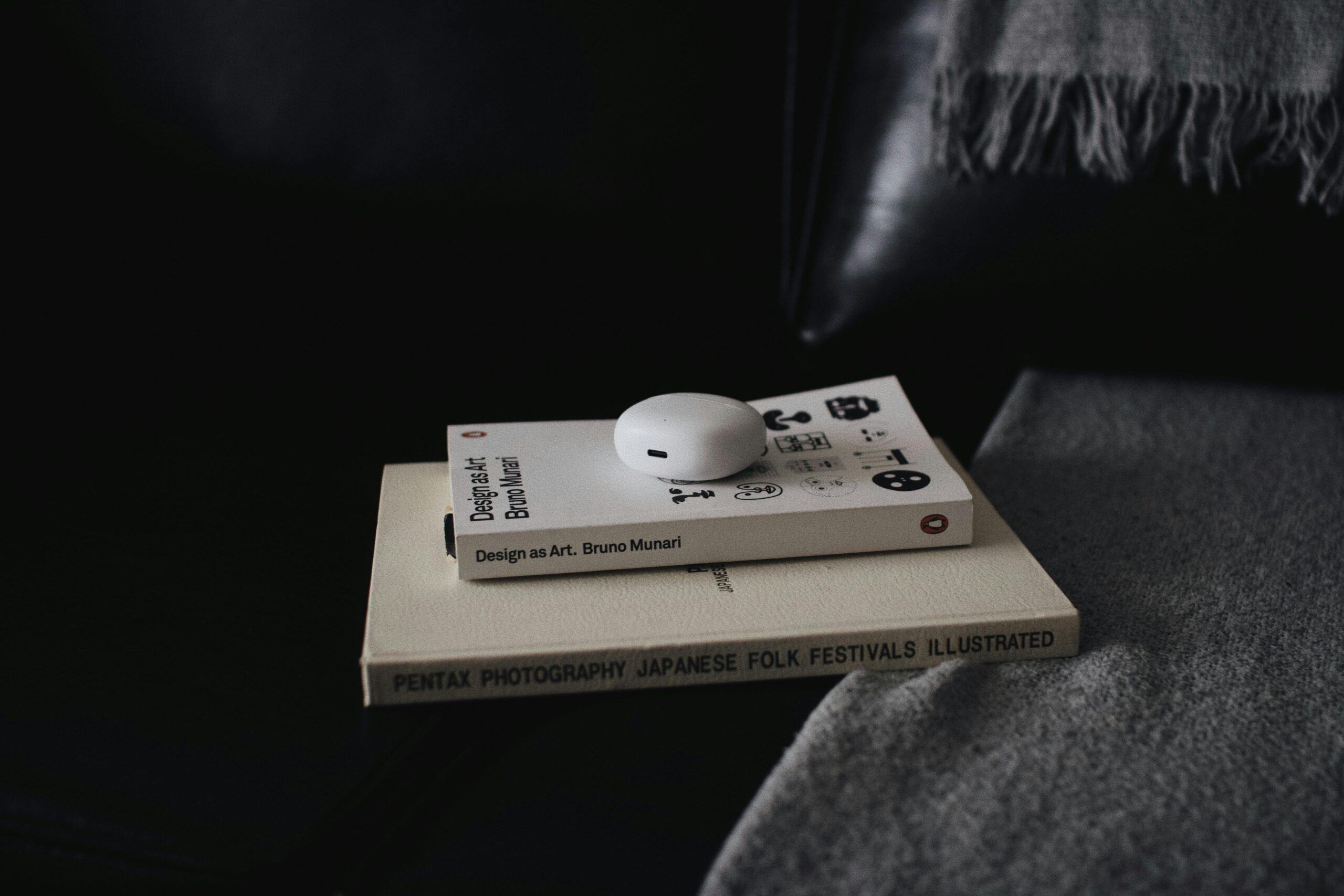 Close-up of books with wireless earbuds on a couch in São Paulo, creating a cozy indoor setting.