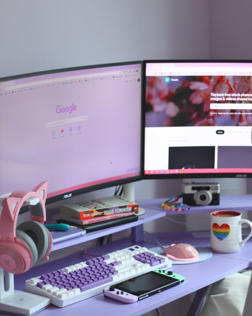 Stylish desk setup with dual monitors, keyboard, headphones, and cozy decor for tech enthusiasts.