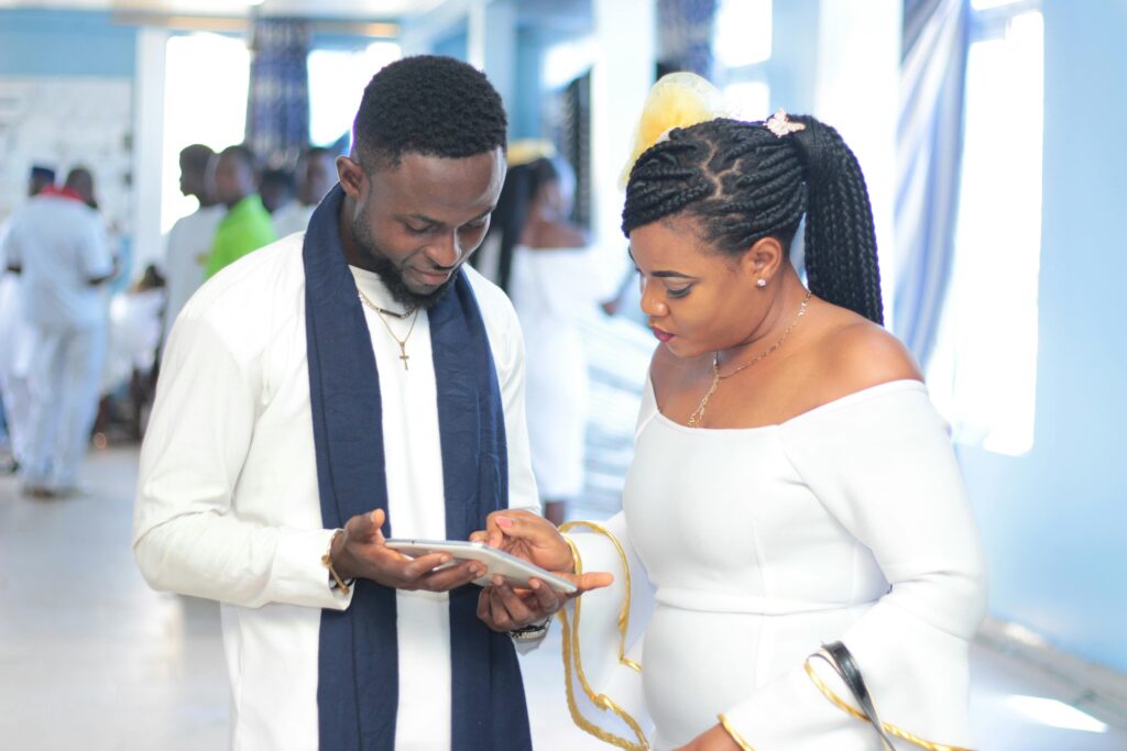 African man and woman engaging with a tablet indoors, dressed elegantly in white.