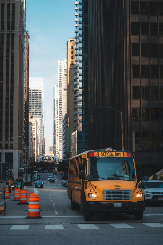 A yellow school bus navigates downtown amidst city skyscrapers and traffic.