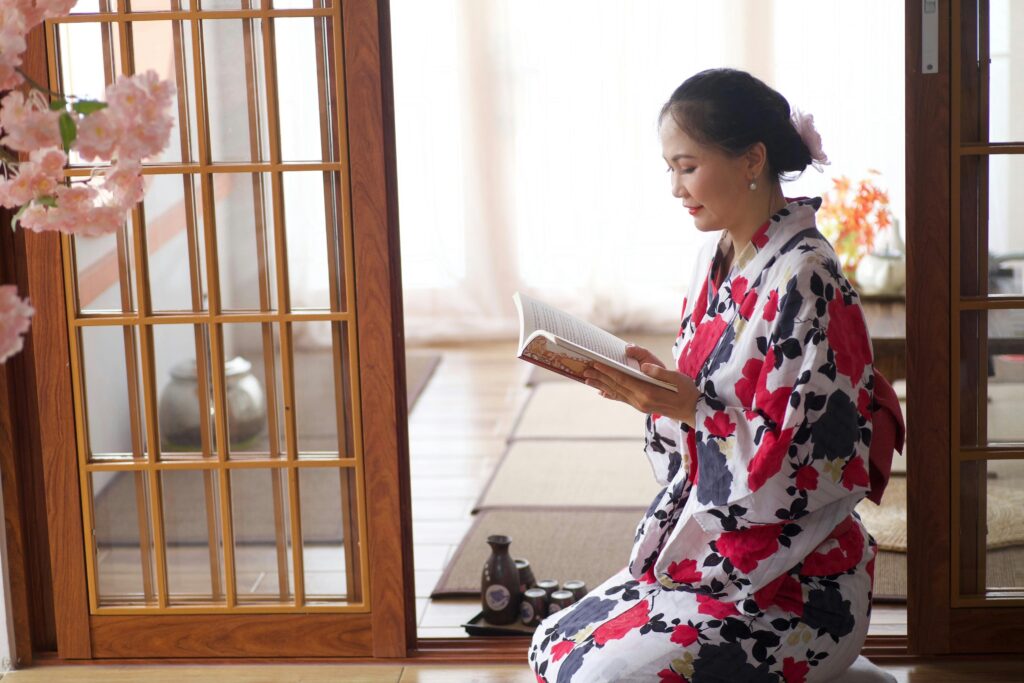 A woman in a floral kimono reads a book inside a Japanese-style room.