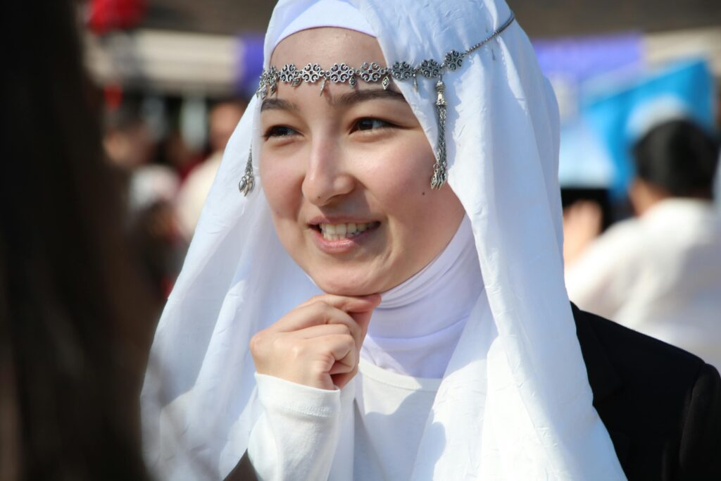 A smiling woman in traditional white Turkish attire with decorative headpiece, outdoors in Antalya, Türkiye.