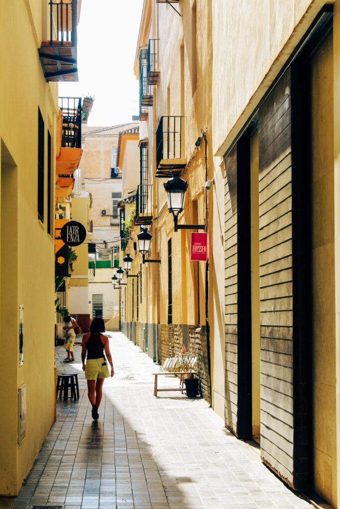 A person walks in a sunlit alleyway in Málaga, Spain, showcasing charming architecture.