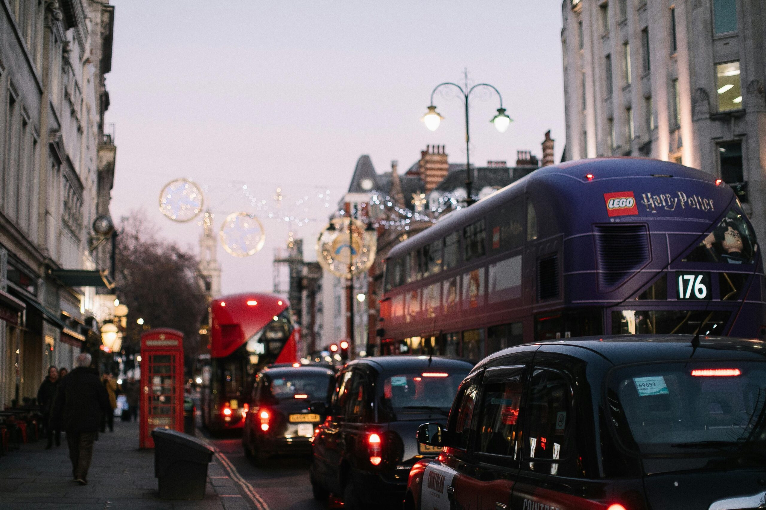 Busy London street scene featuring iconic double-decker buses, cars, and city architecture at dusk.