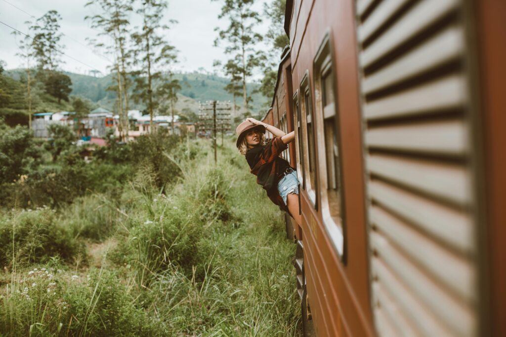 A young woman in casual attire enjoys a scenic train ride through lush countryside.