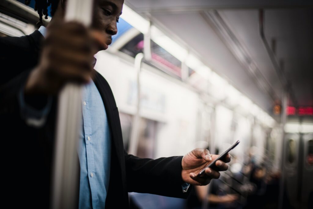 A well-dressed man commuting on a subway train focuses on his smartphone.