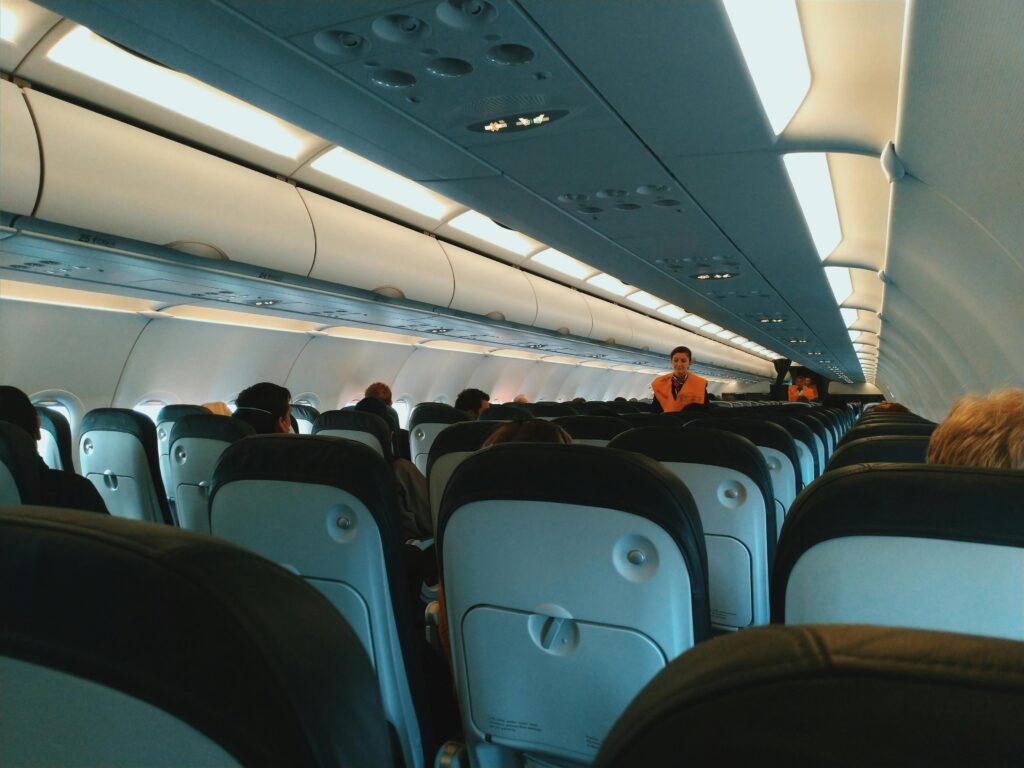 Inside of modern airplane cabin with passengers sitting on comfortable seats and cabin crew standing at passageway