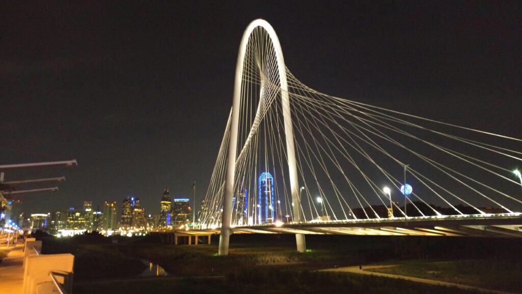 Iconic Dallas skyline featuring the illuminated Margaret Hunt Hill Bridge at night.