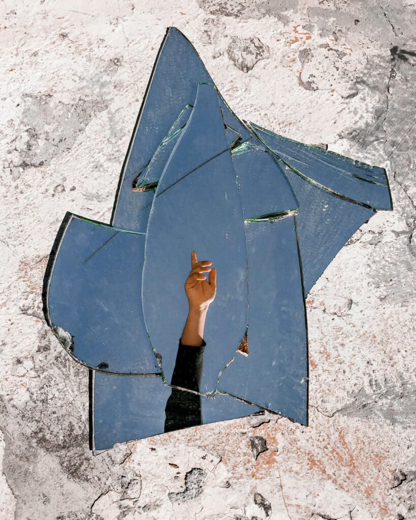 A hand reflected in shattered mirror pieces creates an artistic visual on a textured wall.