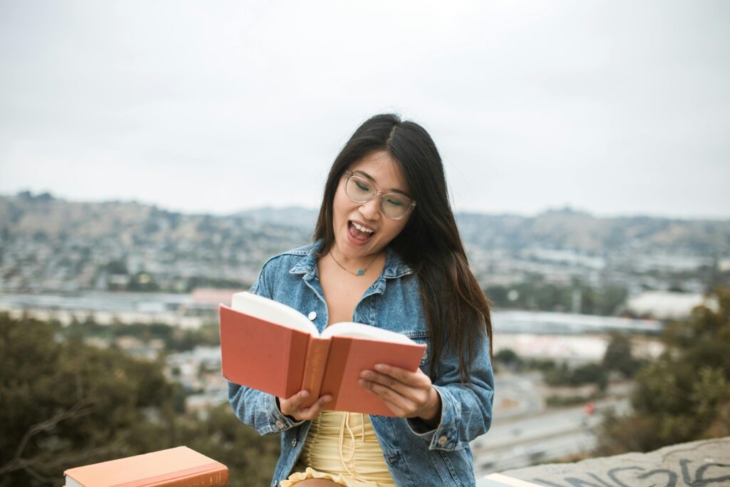 Young woman in a denim jacket enjoys reading a book outdoors.