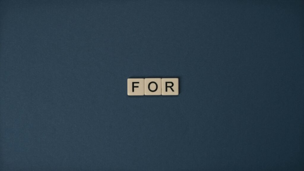 Artistic display of Scrabble tiles spelling the word 'For' on a dark background.