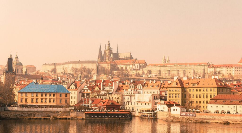 Prague Castle with historic buildings reflected in the Vltava River on a foggy day.