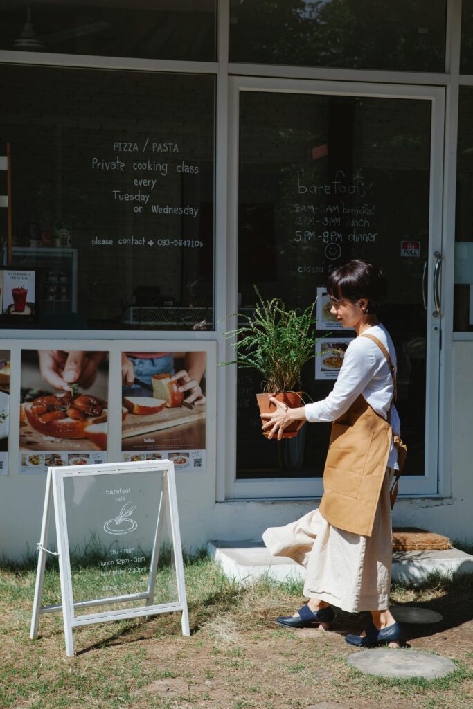 Woman holding a potted plant in front of a café with signage, in daylight.