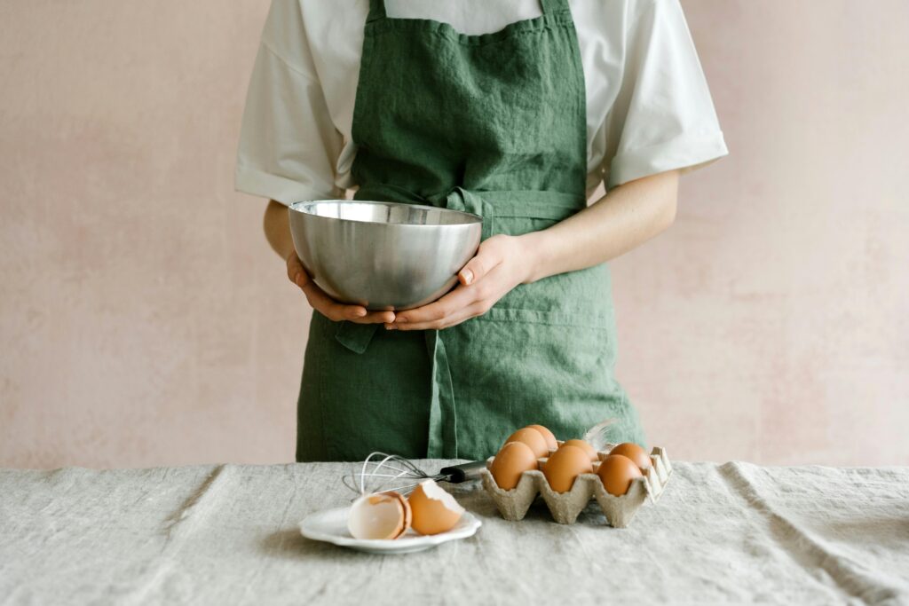 Chef in green apron holding a stainless steel bowl with eggs, ready for baking preparation.