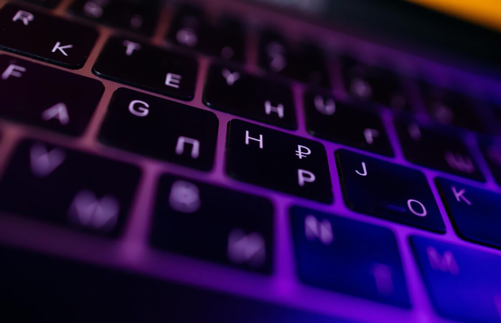 Close-up of a keyboard featuring Cyrillic letters and symbols, illuminated by purple light.